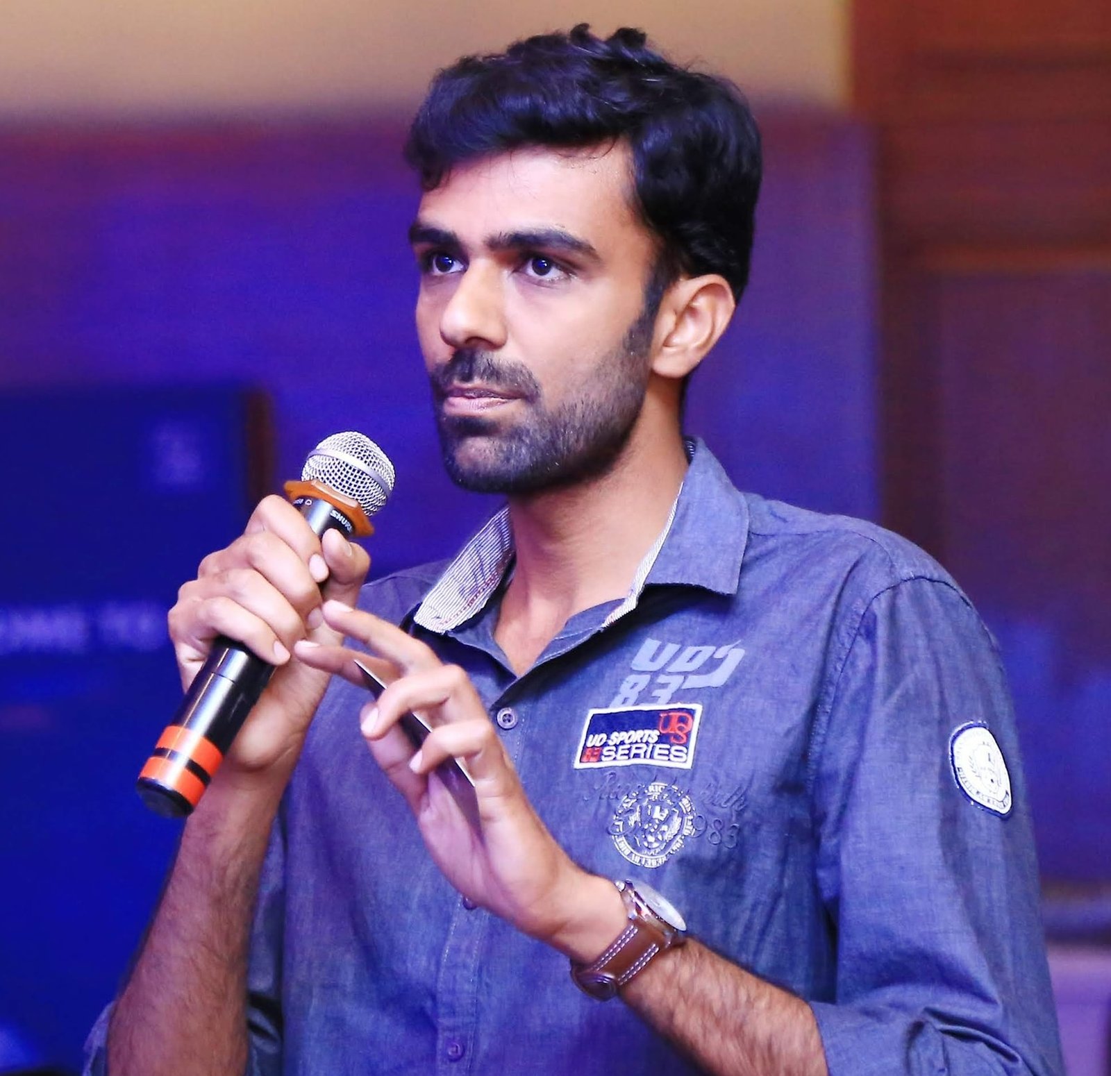 Nesamani Elangovan speaking into a microphone at an event